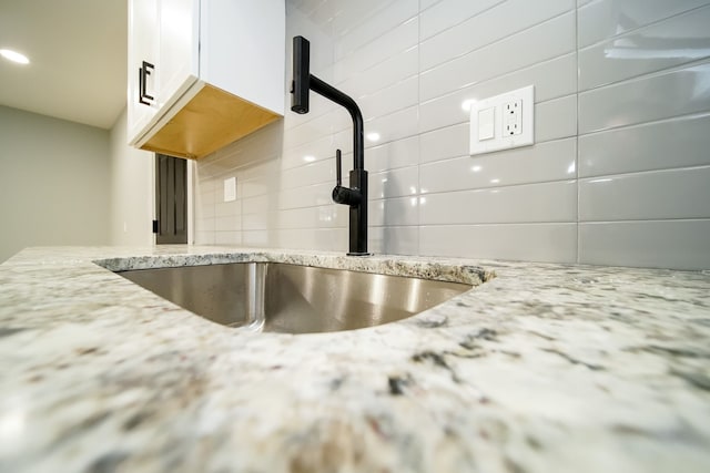 interior details featuring tasteful backsplash, light stone counters, sink, and white cabinets