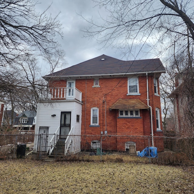 rear view of house featuring brick siding, fence, and a balcony