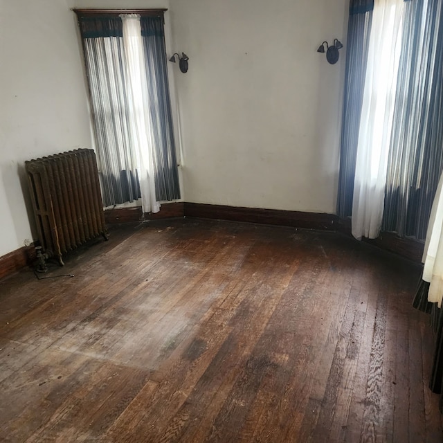 empty room with radiator heating unit, baseboards, and hardwood / wood-style floors