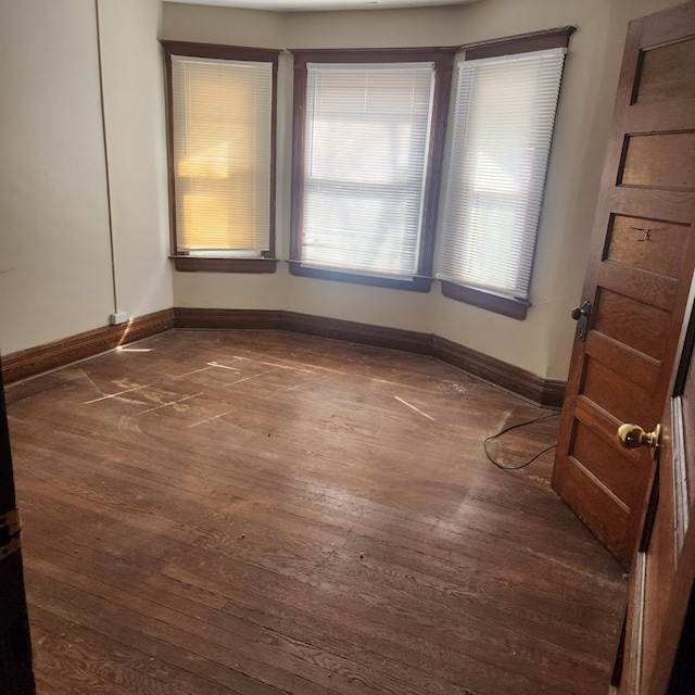 unfurnished room featuring baseboards and dark wood-type flooring