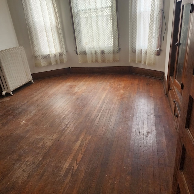 empty room featuring radiator, wood-type flooring, and baseboards