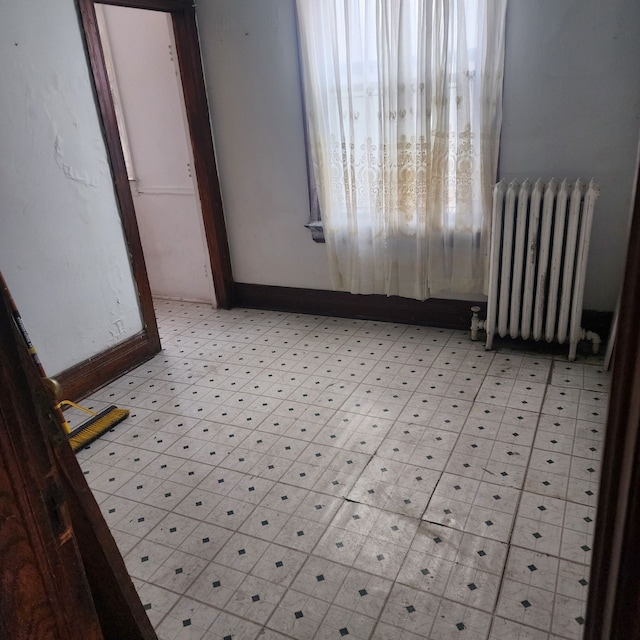 empty room featuring light floors, baseboards, and radiator heating unit