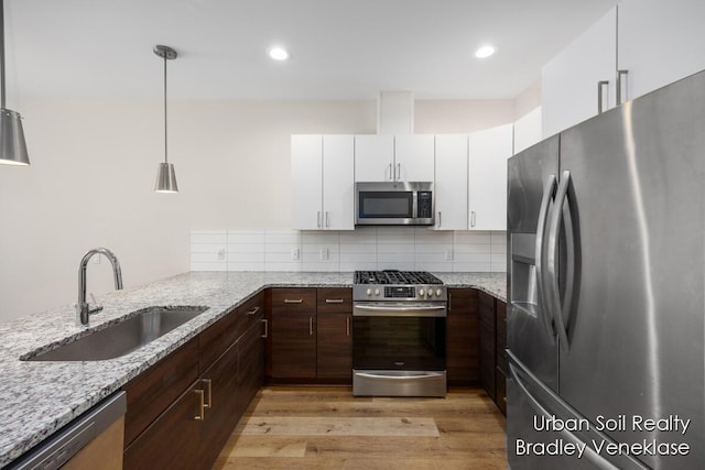 kitchen featuring white cabinetry, stainless steel appliances, decorative light fixtures, light stone countertops, and sink