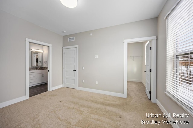 unfurnished bedroom with ensuite bathroom, a closet, carpet flooring, and a spacious closet