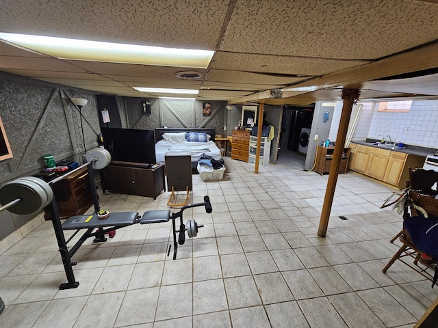 basement with sink, light tile patterned floors, a drop ceiling, and washer / dryer