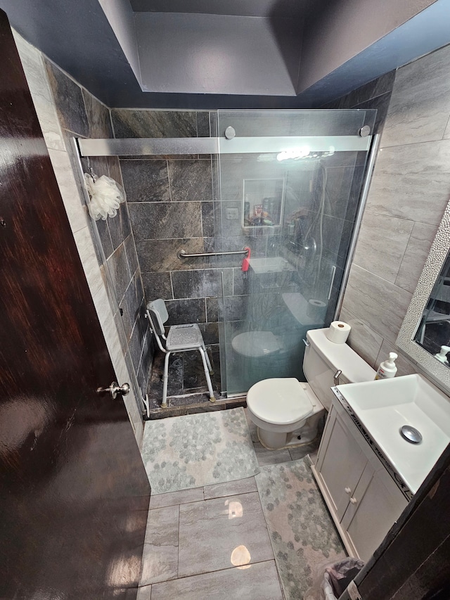 bathroom with tile patterned floors, vanity, tile walls, toilet, and a shower with shower door