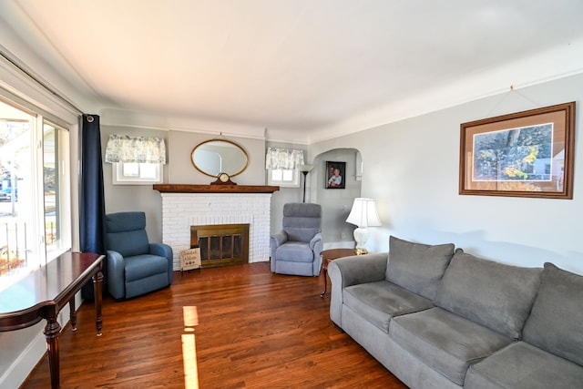 living room featuring ornamental molding, dark hardwood / wood-style floors, a brick fireplace, and a healthy amount of sunlight