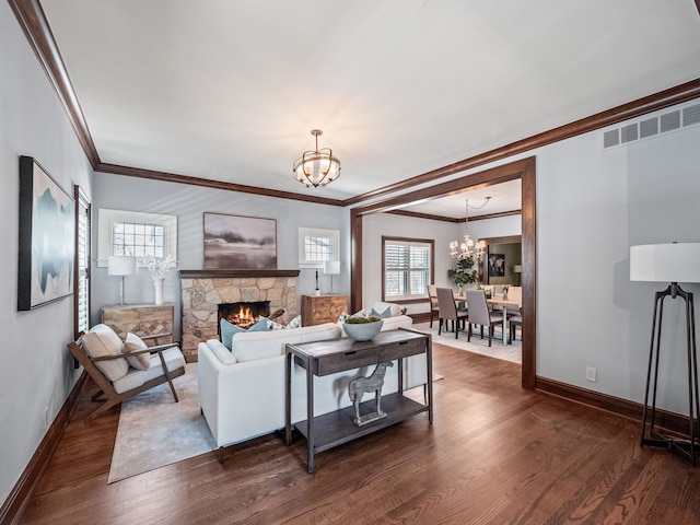 living room with a notable chandelier, a stone fireplace, dark wood-type flooring, and crown molding