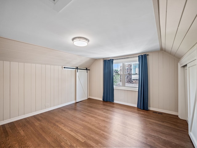 bonus room featuring a barn door, wood walls, wood-type flooring, and vaulted ceiling