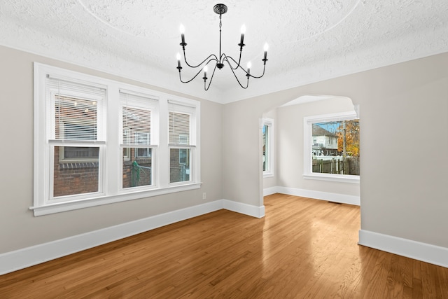 unfurnished dining area with wood-type flooring, a textured ceiling, and a notable chandelier