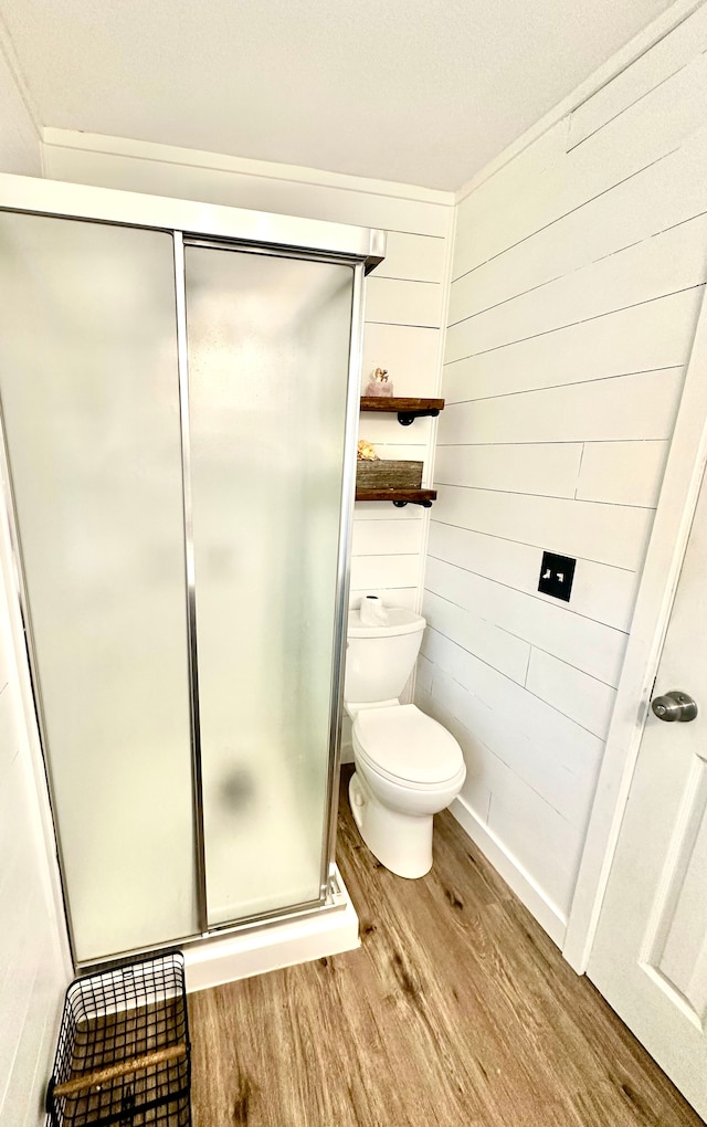 bathroom featuring wooden walls, wood-type flooring, a shower with shower door, and toilet