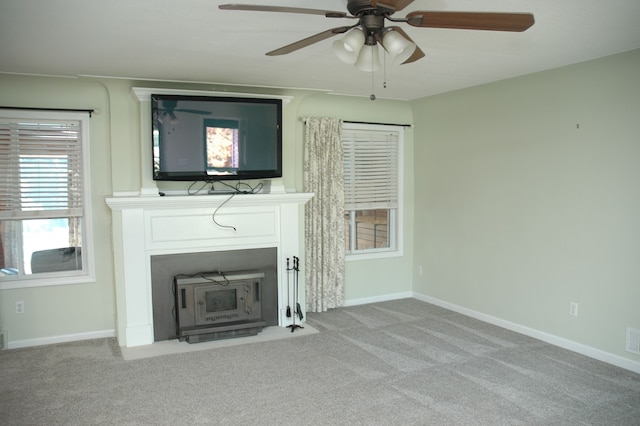 unfurnished living room featuring ceiling fan, a wood stove, and light carpet