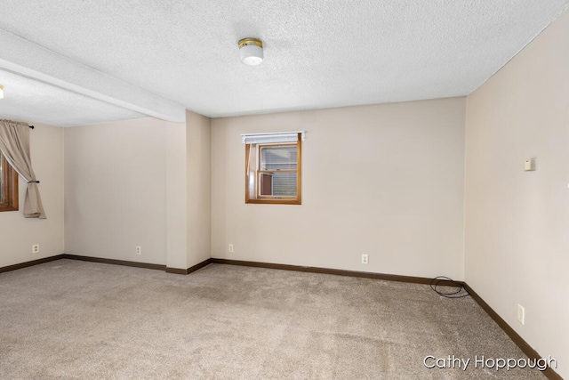 empty room with light colored carpet, a textured ceiling, and baseboards