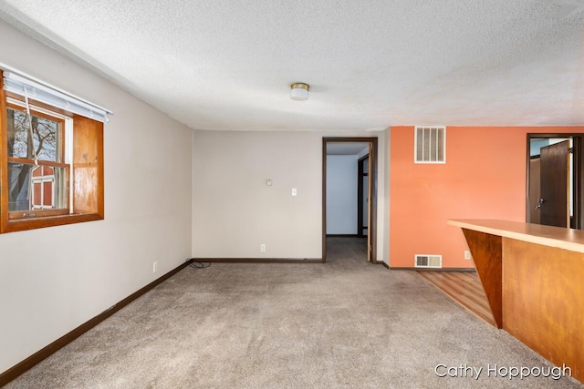 empty room with baseboards, visible vents, a textured ceiling, and carpet flooring