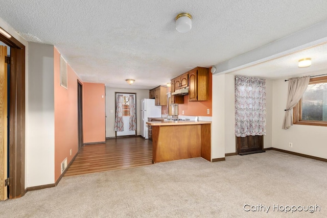 kitchen featuring light colored carpet, a peninsula, light countertops, freestanding refrigerator, and brown cabinetry