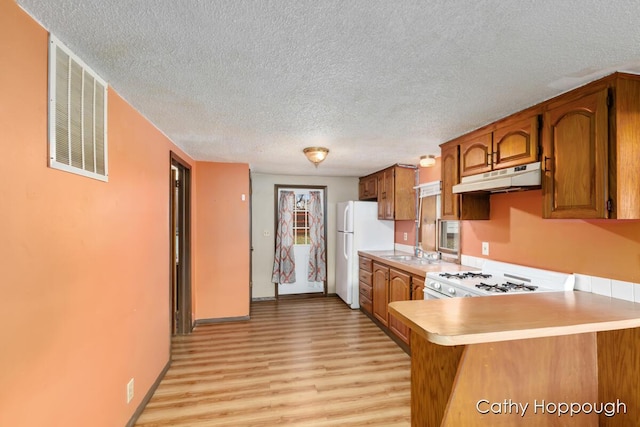 kitchen with white appliances, brown cabinetry, a peninsula, light countertops, and under cabinet range hood