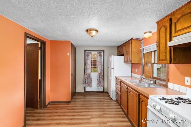 kitchen with white appliances, brown cabinetry, light countertops, light wood-type flooring, and a sink