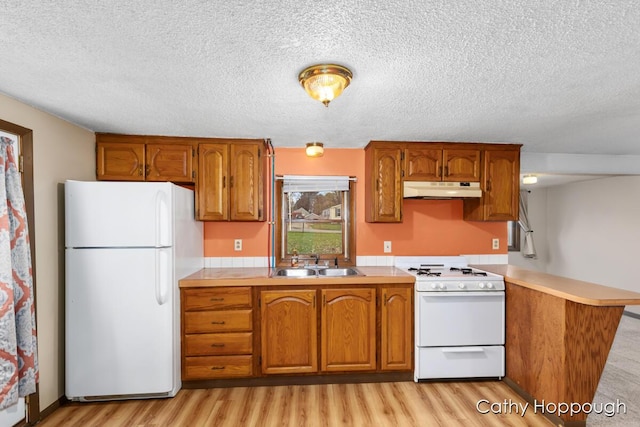 kitchen featuring white appliances, brown cabinetry, light countertops, under cabinet range hood, and a sink