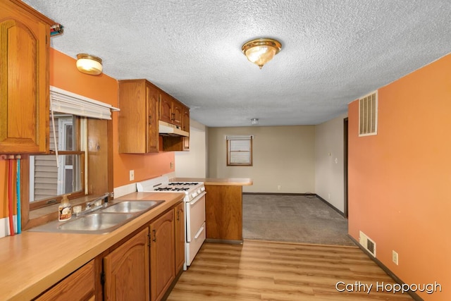 kitchen with under cabinet range hood, white gas range oven, light countertops, and a sink