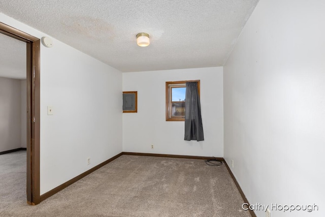 empty room featuring electric panel, light colored carpet, a textured ceiling, and baseboards