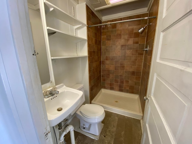 bathroom with a tile shower, toilet, and sink