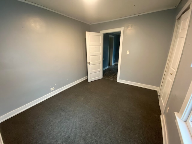 unfurnished bedroom featuring dark carpet, a closet, and ornamental molding