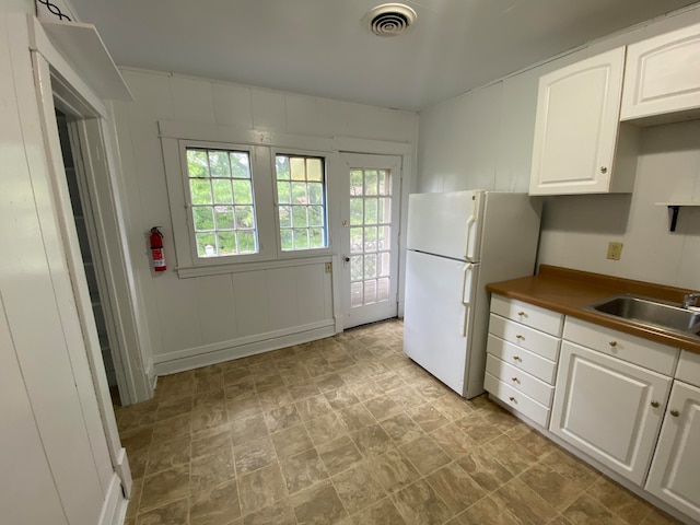 kitchen with white fridge, white cabinetry, and sink