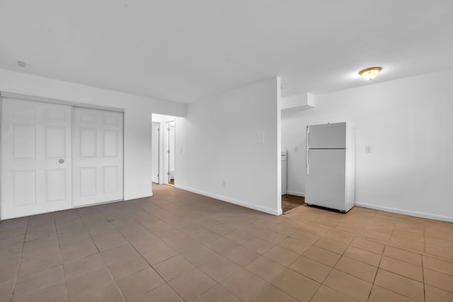 unfurnished bedroom featuring white refrigerator, light tile patterned floors, and a closet