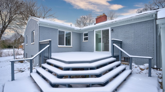 snow covered property with brick siding and a chimney