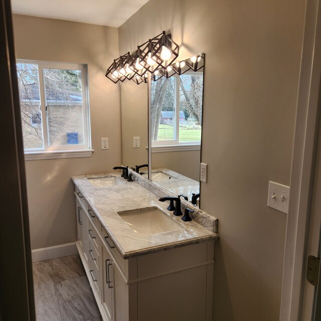 bathroom featuring double vanity, marble finish floor, baseboards, and a sink