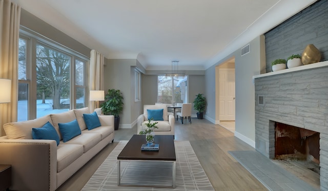 living area with a stone fireplace, light wood-style flooring, visible vents, baseboards, and ornamental molding