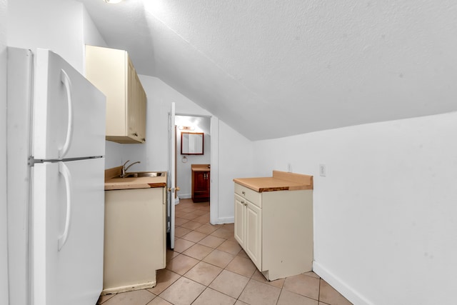 kitchen with sink, white fridge, lofted ceiling, cream cabinetry, and light tile patterned floors