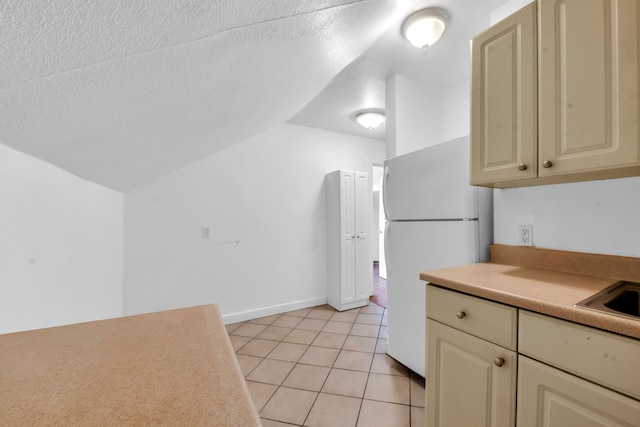 kitchen with cream cabinetry, white refrigerator, lofted ceiling, and a textured ceiling