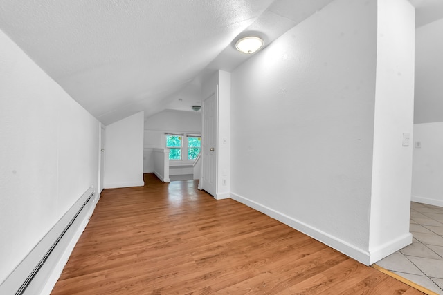 bonus room with vaulted ceiling, light hardwood / wood-style flooring, a textured ceiling, and a baseboard heating unit