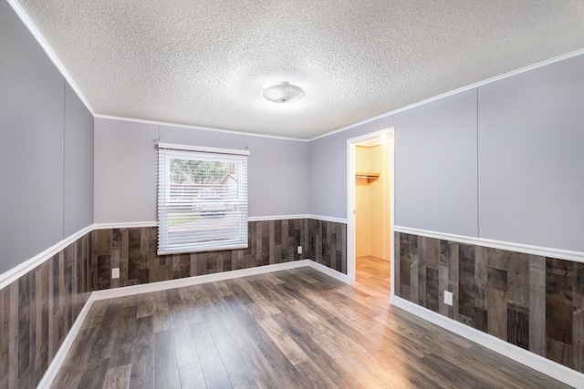 unfurnished room featuring hardwood / wood-style flooring, wood walls, crown molding, and a textured ceiling