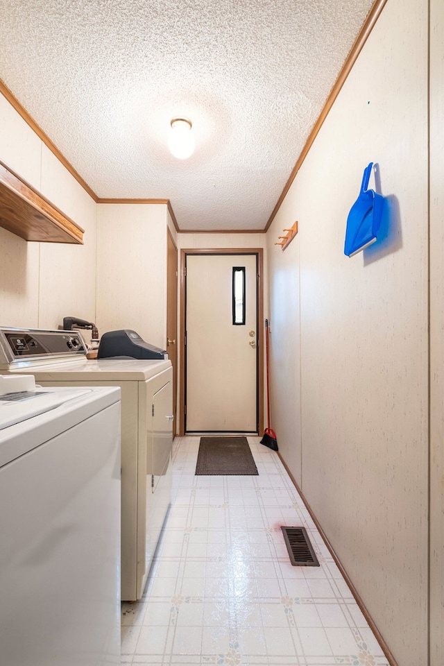 laundry area featuring a textured ceiling, ornamental molding, and washing machine and clothes dryer