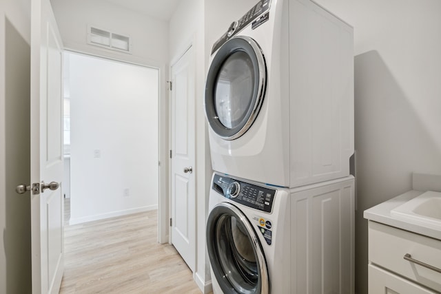 washroom featuring cabinets, light hardwood / wood-style floors, and stacked washer and clothes dryer