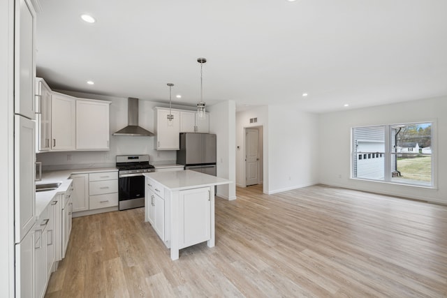 kitchen with stainless steel appliances, wall chimney range hood, pendant lighting, light hardwood / wood-style floors, and a kitchen island