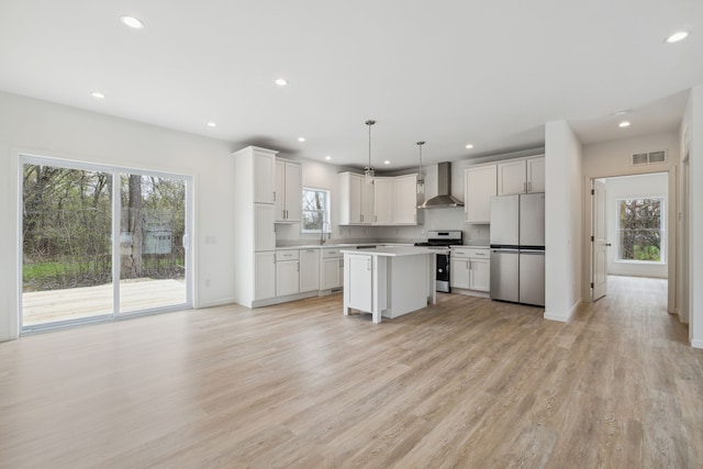 kitchen featuring stainless steel appliances, wall chimney range hood, decorative light fixtures, a center island, and plenty of natural light