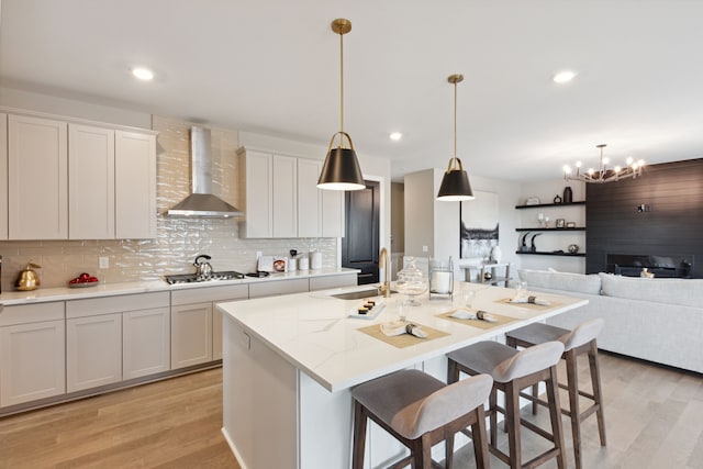 kitchen featuring pendant lighting, light hardwood / wood-style floors, a center island with sink, and wall chimney range hood