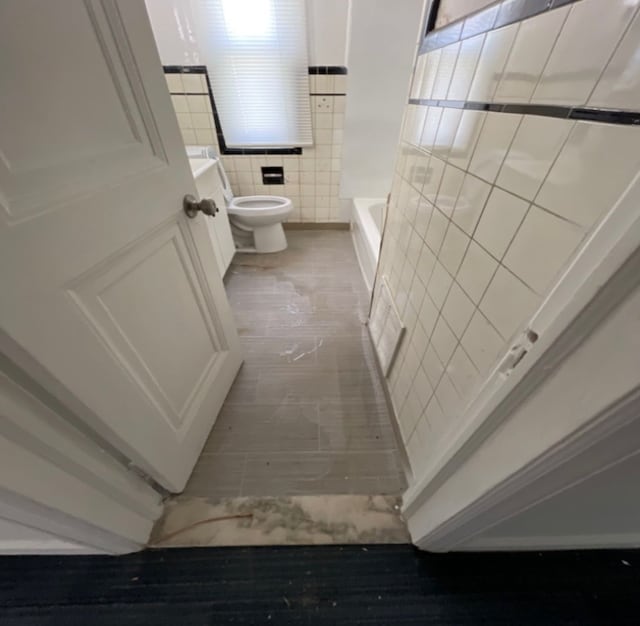 bathroom featuring a bathing tub, toilet, tile walls, and hardwood / wood-style floors