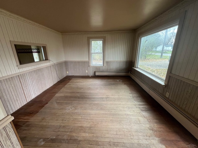 empty room with hardwood / wood-style floors, a baseboard radiator, and a healthy amount of sunlight