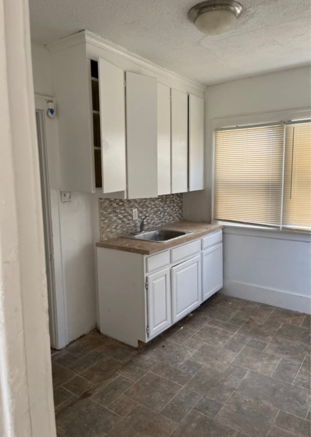 kitchen with backsplash, white cabinetry, and sink