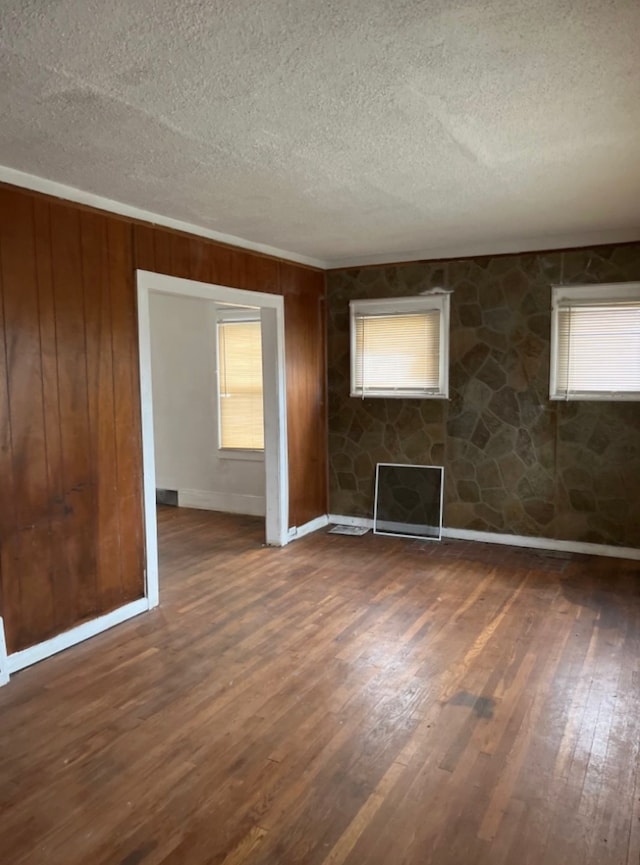 empty room with a textured ceiling, dark hardwood / wood-style flooring, and wooden walls