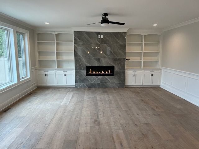 unfurnished living room with crown molding, built in shelves, wood finished floors, and a wealth of natural light