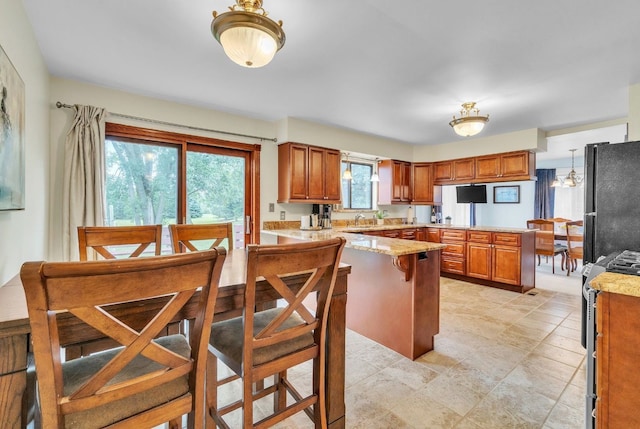 kitchen featuring kitchen peninsula, black refrigerator, sink, pendant lighting, and stainless steel gas stove