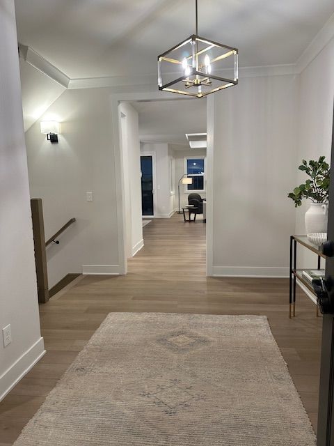 hallway featuring crown molding, wood-type flooring, and an inviting chandelier