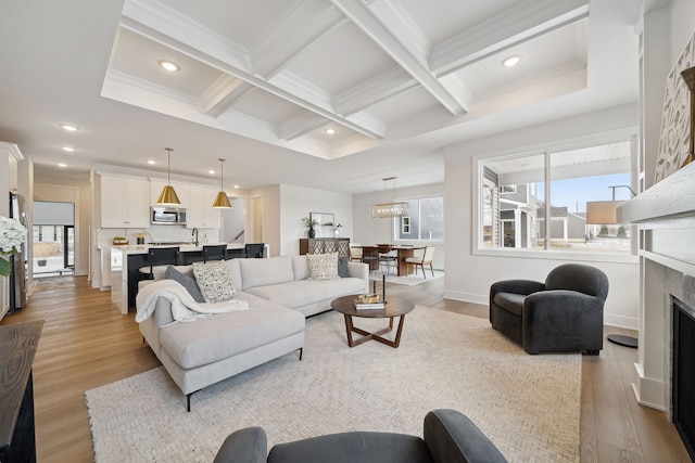 living room featuring light wood-type flooring, a fireplace, coffered ceiling, and beamed ceiling