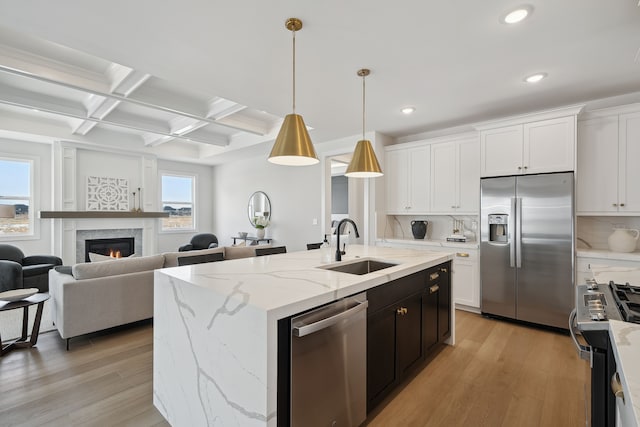 kitchen with hanging light fixtures, appliances with stainless steel finishes, open floor plan, white cabinetry, and a sink