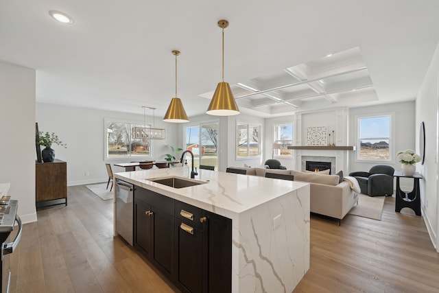 kitchen featuring an island with sink, light stone counters, open floor plan, stainless steel dishwasher, and a sink